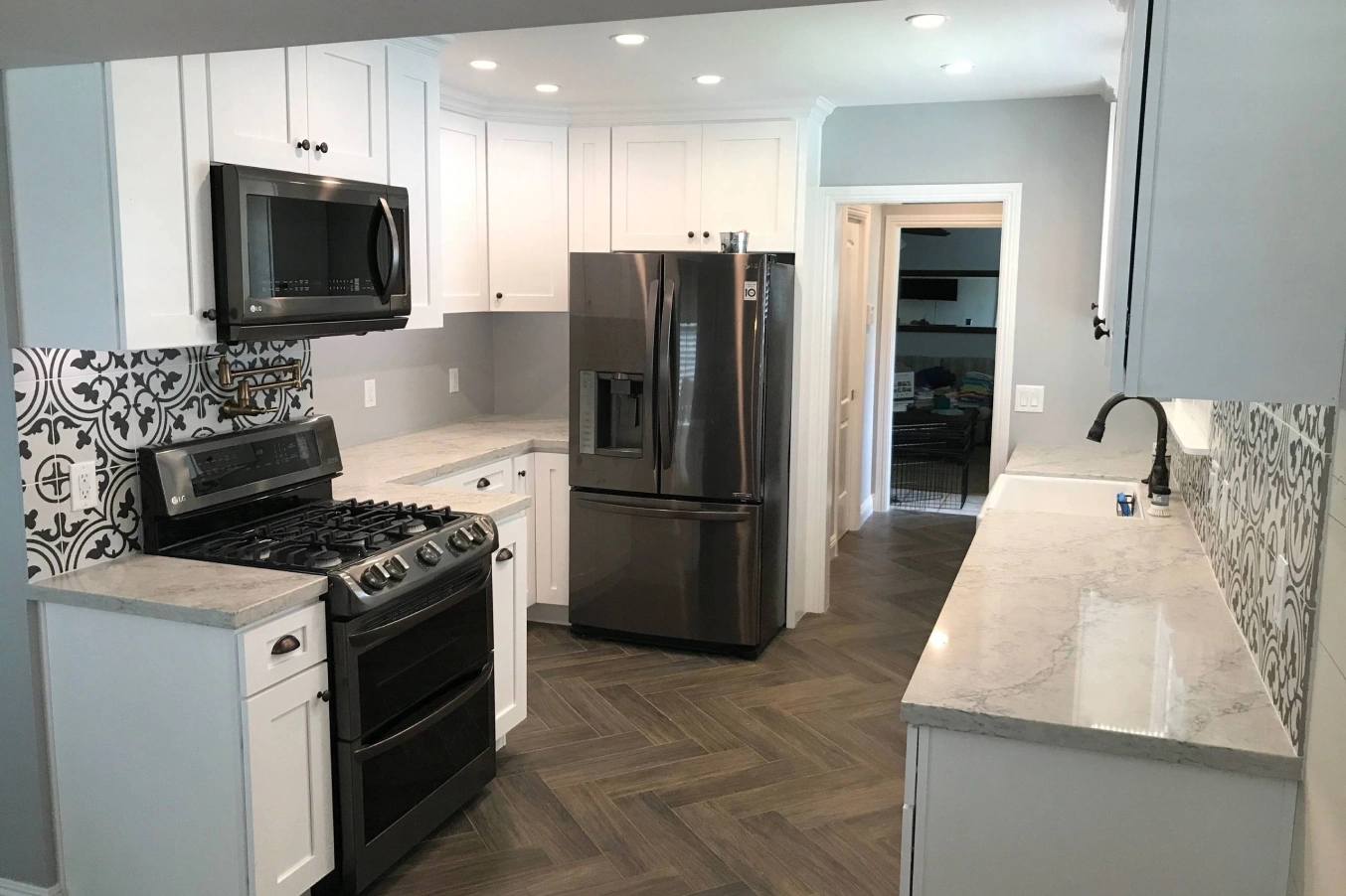Modern kitchen with stainless steel appliances, white cabinets, patterned backsplash, and herringbone tile floor.