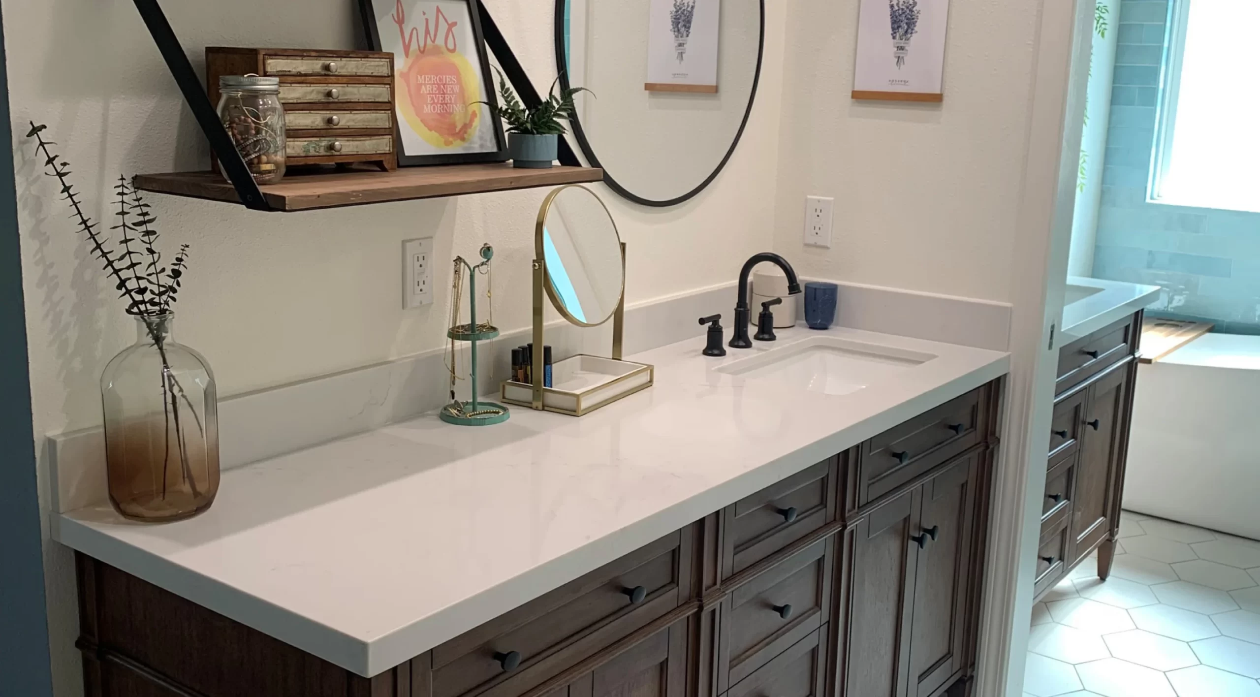 bathroom-remodel-cta A bathroom vanity with a round mirror, wooden cabinets, and decor on shelves. A sink and faucet are on the white countertop.