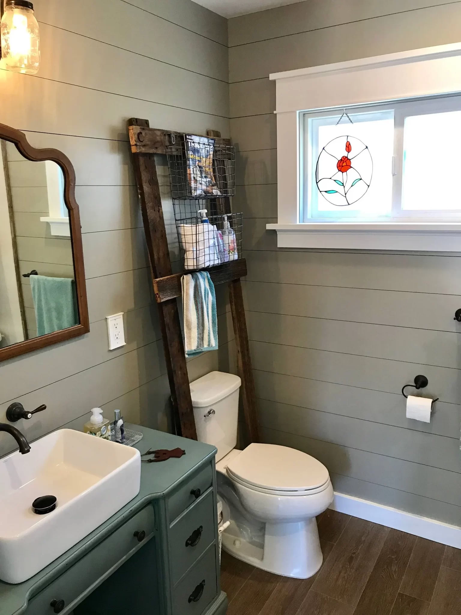 bathroom-remodels-1 Bathroom with a sink, toilet, ladder shelf, and a window with stained glass art above the toilet.