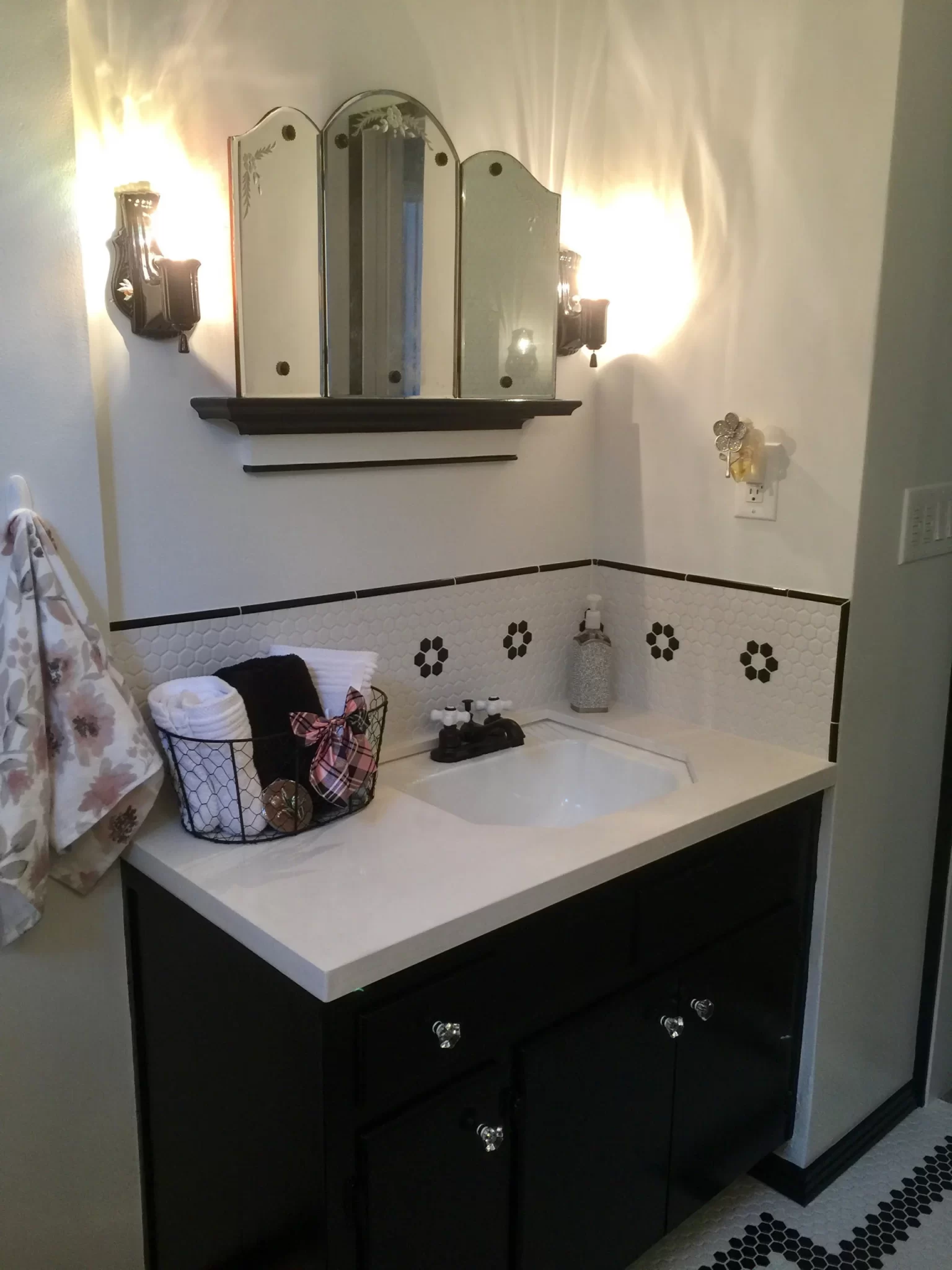 bathroom-remodels-4 Bathroom vanity with black cabinets, a mirror, towel, and toiletries, lit by two wall sconces.