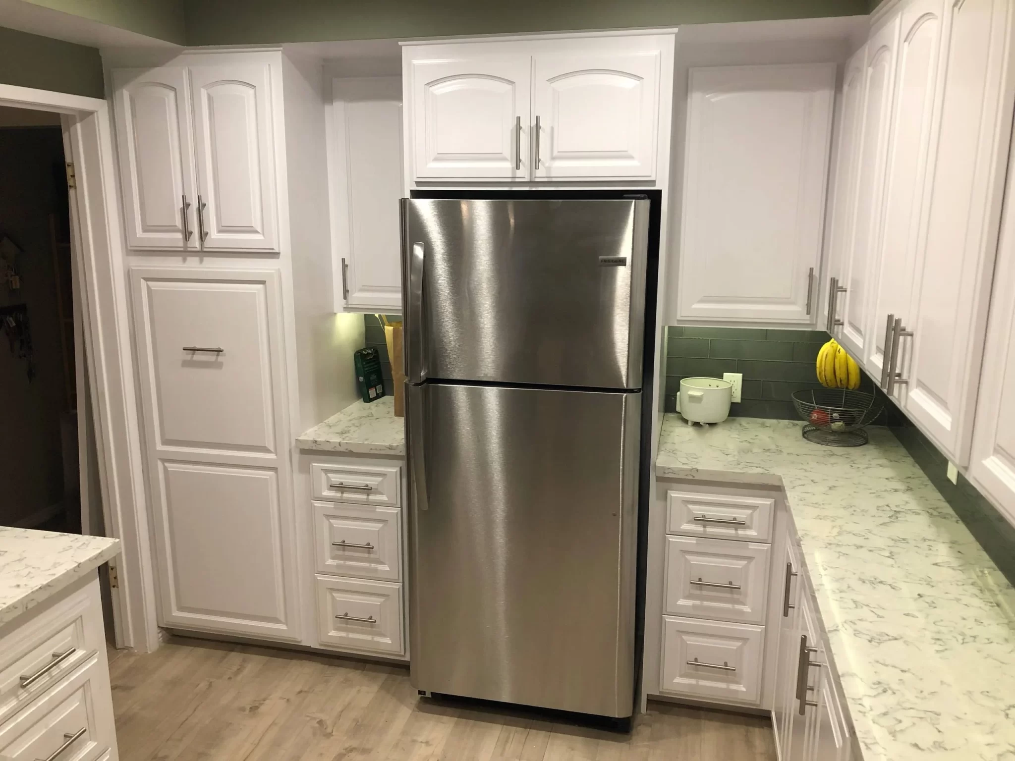 custom-cabinetry-carpentry-10 A modern kitchen with white cabinets, marble countertops, and a stainless steel refrigerator.