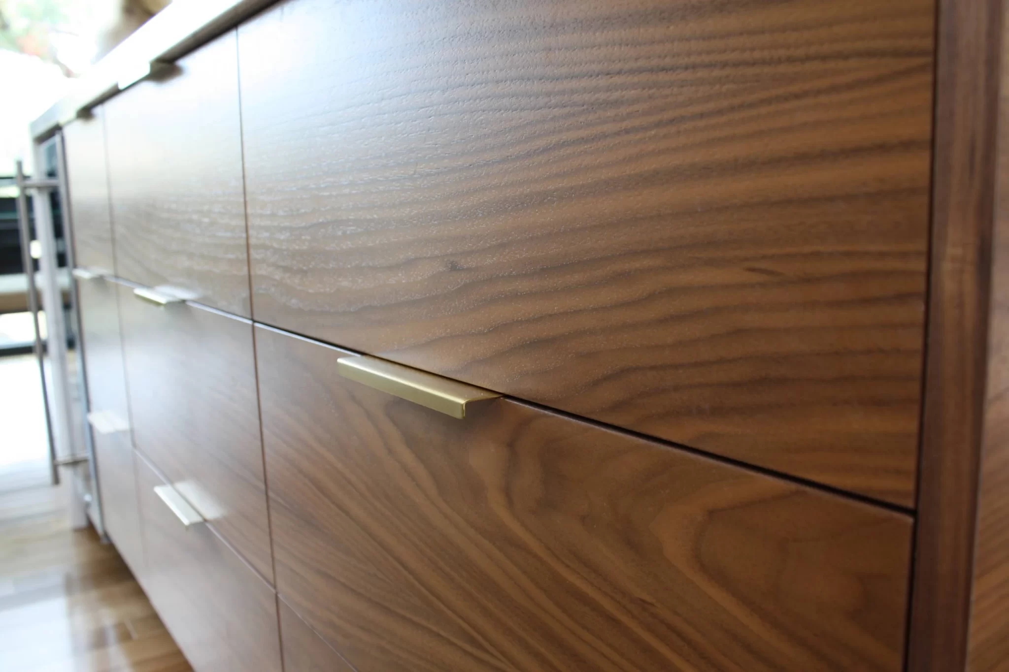 custom-cabinetry-carpentry-12 Close-up of wooden kitchen cabinets with modern metal handles and visible wood grain.