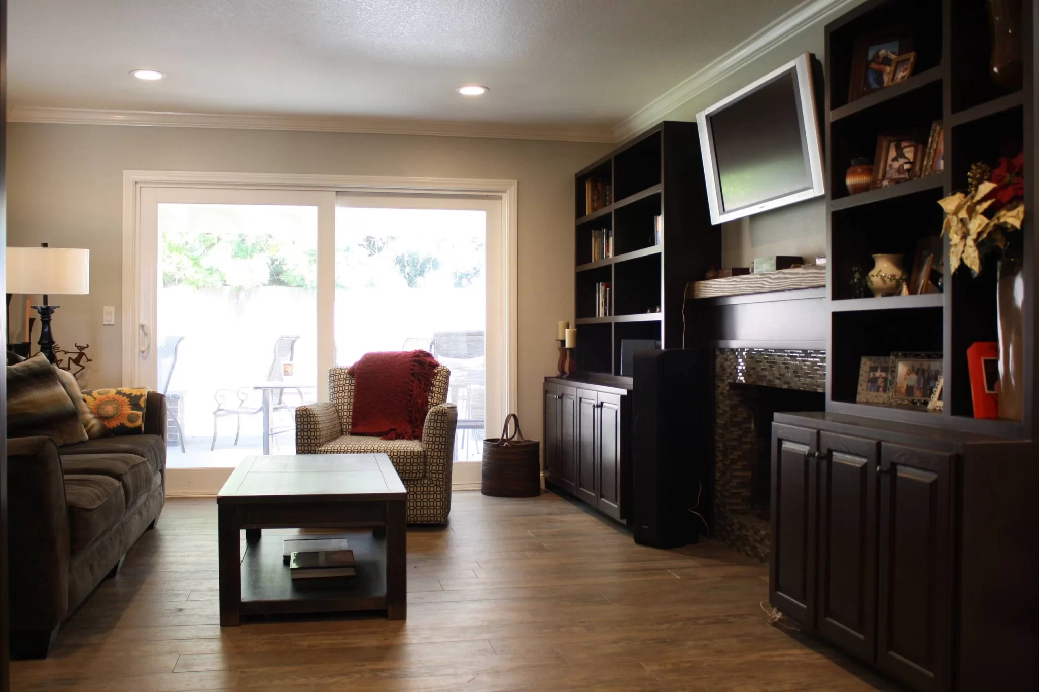 custom-cabinetry-carpentry-13 Modern living room with dark wood shelves, a gray sofa, armchair, coffee table, and sliding glass doors.