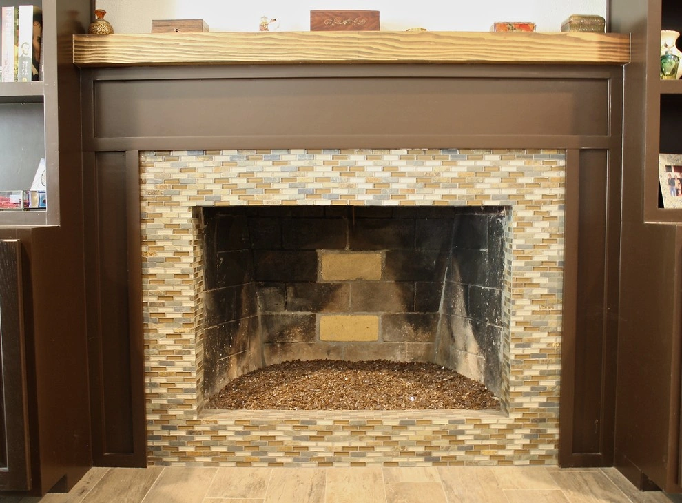 custom-cabinetry-carpentry-14 A fireplace with a mosaic tile border, empty firebox, and dark wood mantel in a living room.