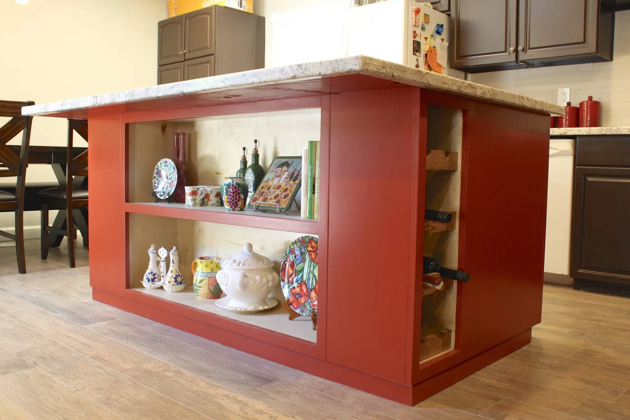 custom-cabinetry-carpentry-15 Red kitchen island with open shelves displaying dishes and wine rack, in a modern kitchen setting.