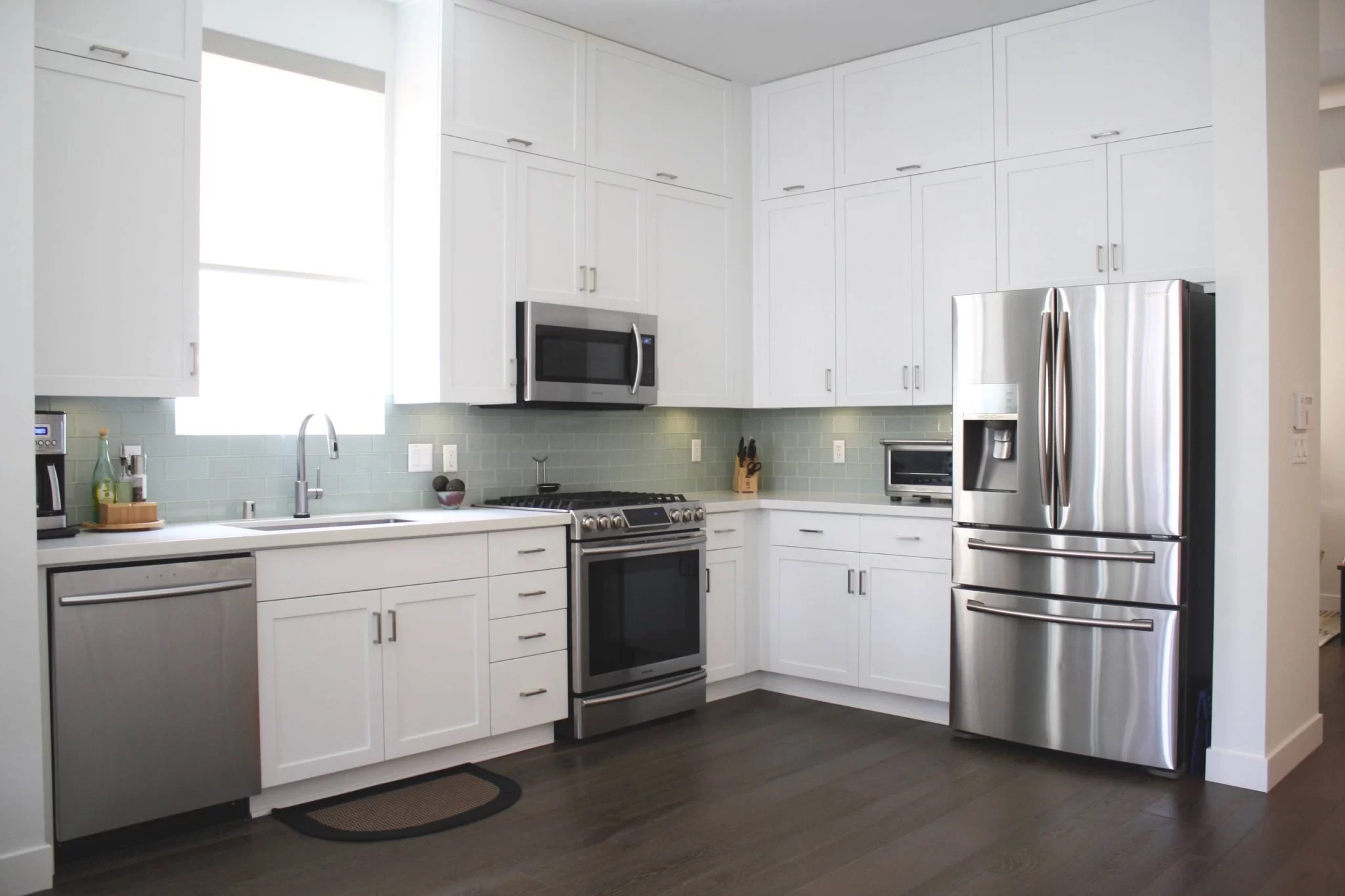 custom-cabinetry-carpentry-3 Modern kitchen with white cabinets, stainless steel appliances, and light blue tile backsplash.
