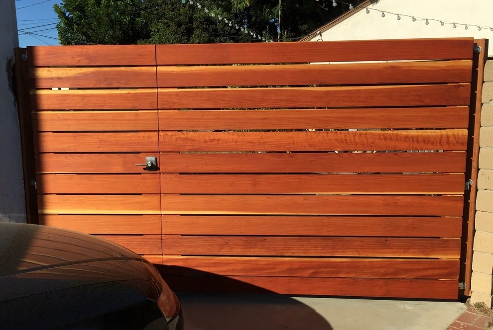 custom-fences-and-gates-2 Horizontal wooden gate with metal lock, partially shaded, next to a car and a brick wall.