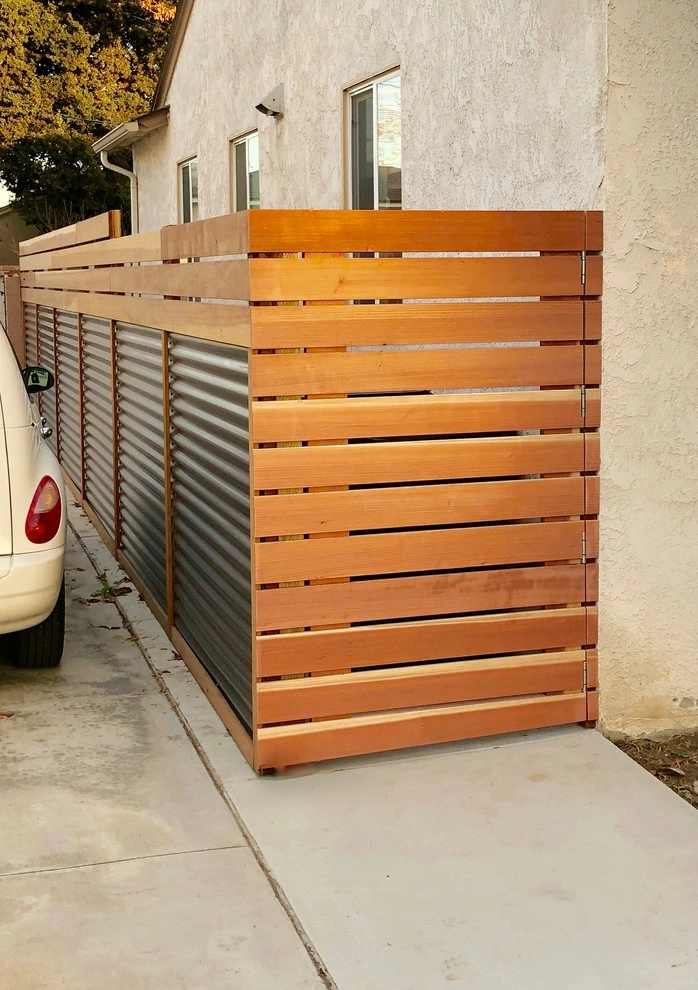 custom-fences-and-gates-5 Modern wooden and metal privacy fence runs alongside a house next to a parked white vehicle.