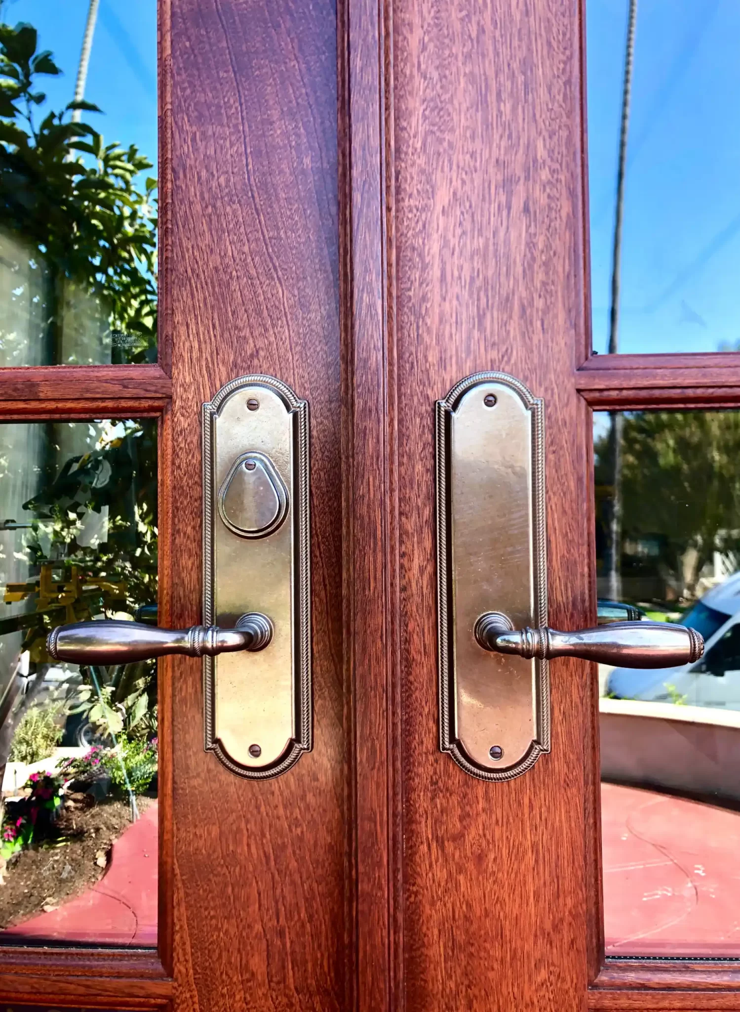 doors-and-windows-2 Two brass door handles on a wooden double door with glass panels, reflecting trees and a car outside.
