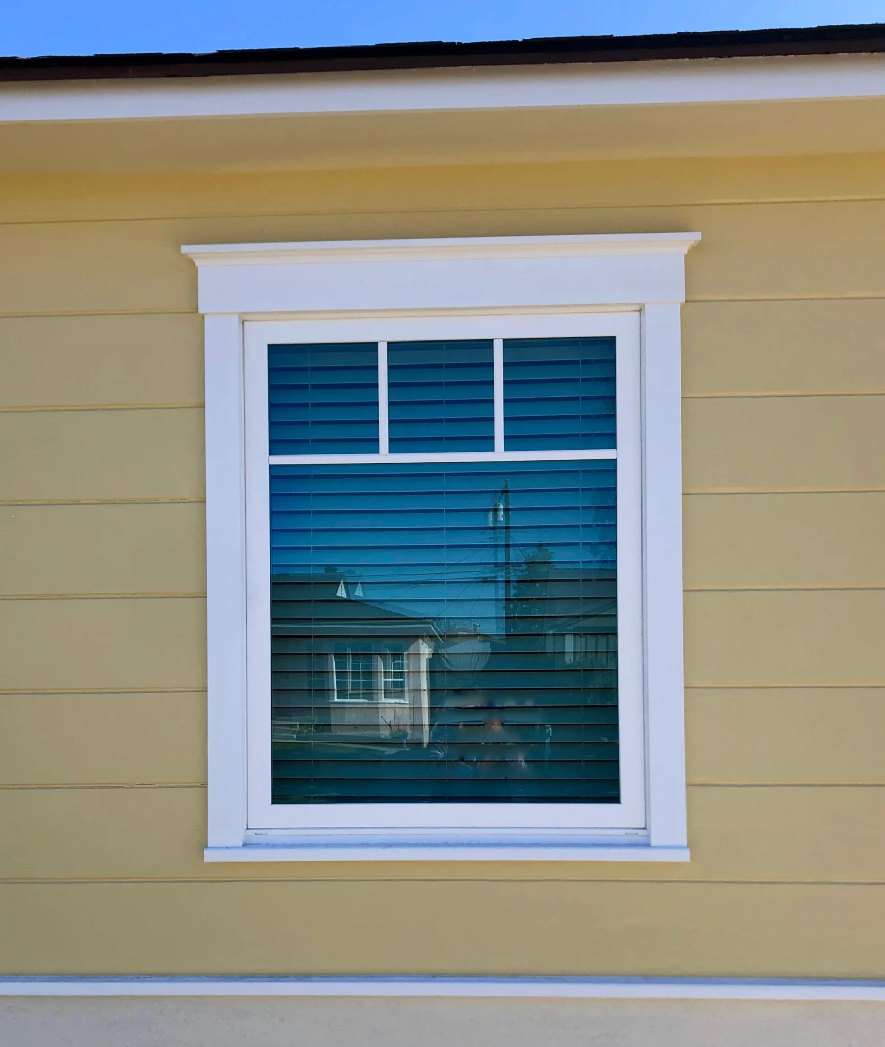 doors-and-windows-6 A yellow house with a white-trimmed window and blue blinds reflecting nearby houses.