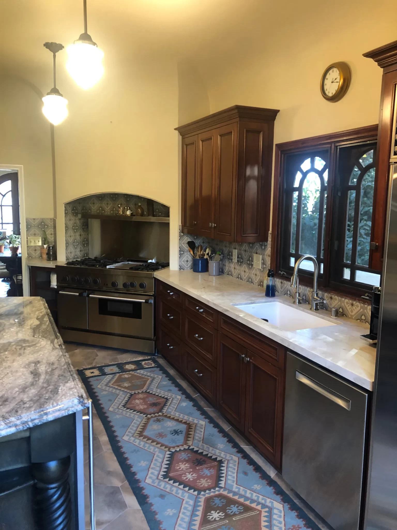 kitchen-remodels-11 Kitchen with dark wood cabinets, patterned rug, marble island, large stove, and arched windows.