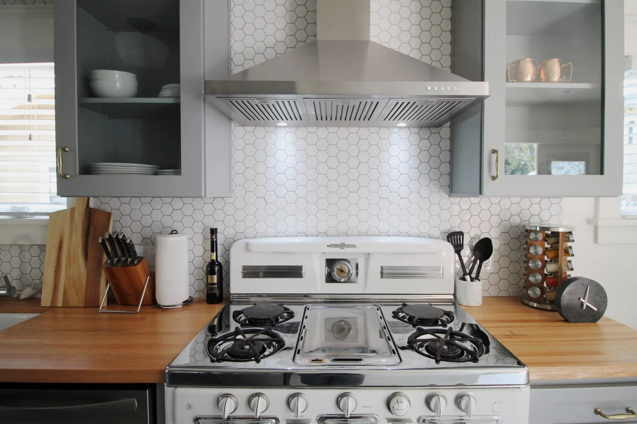 kitchen-remodels-3 Modern kitchen with a gas stove, wooden countertops, utensils, and hexagonal white tile backsplash.