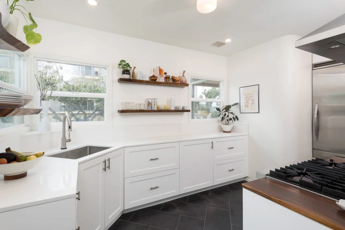 kitchen-remodels-4 Modern white kitchen with open shelves, stainless steel appliances, and a large corner sink by two windows.