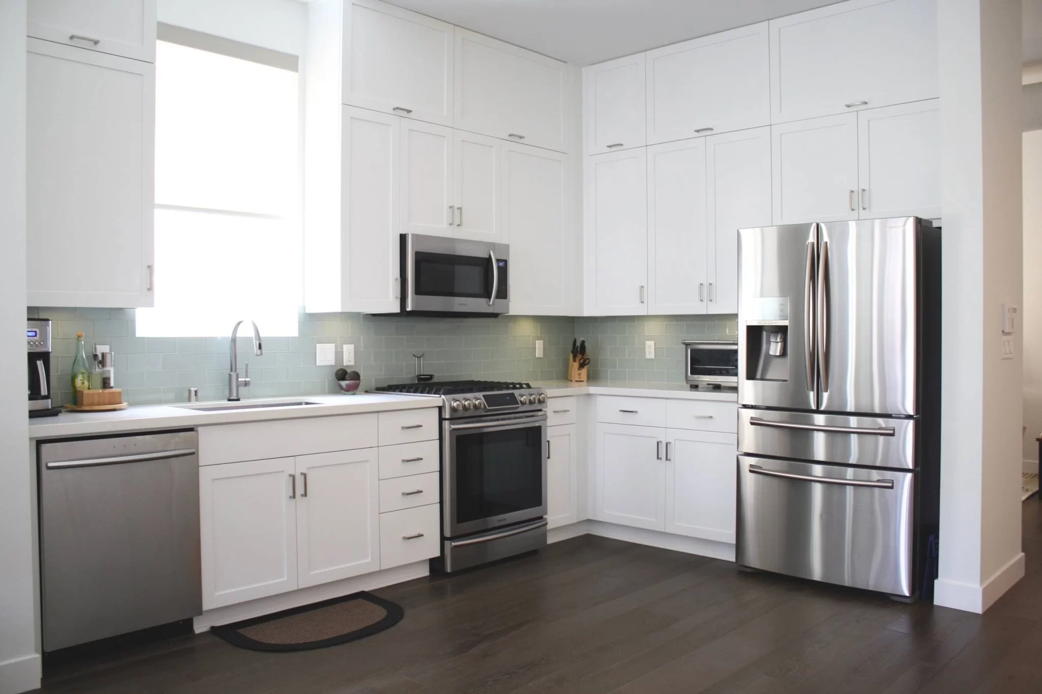 kitchen-remodels-7 Modern kitchen with white cabinets, stainless steel appliances, and a light blue tiled backsplash.