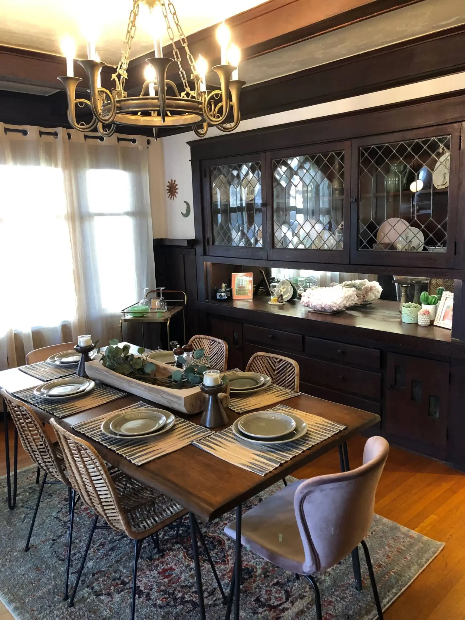 living-spaces-1 A cozy dining room with a wooden table, six chairs, a rug, and a vintage hutch with glass cabinets.