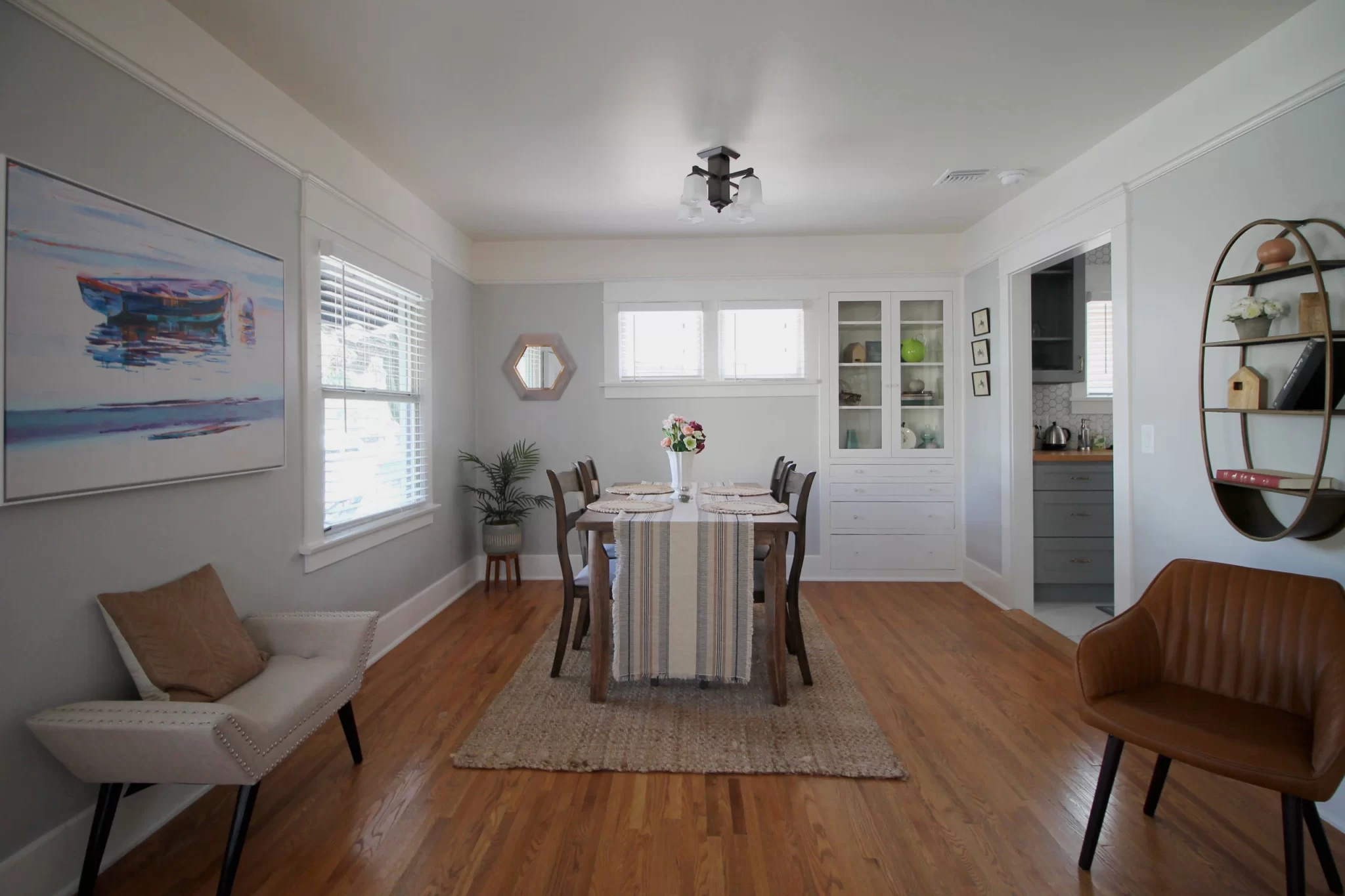 living-spaces-4 Bright dining room with a wooden table, six chairs, wall art, and natural light from windows.