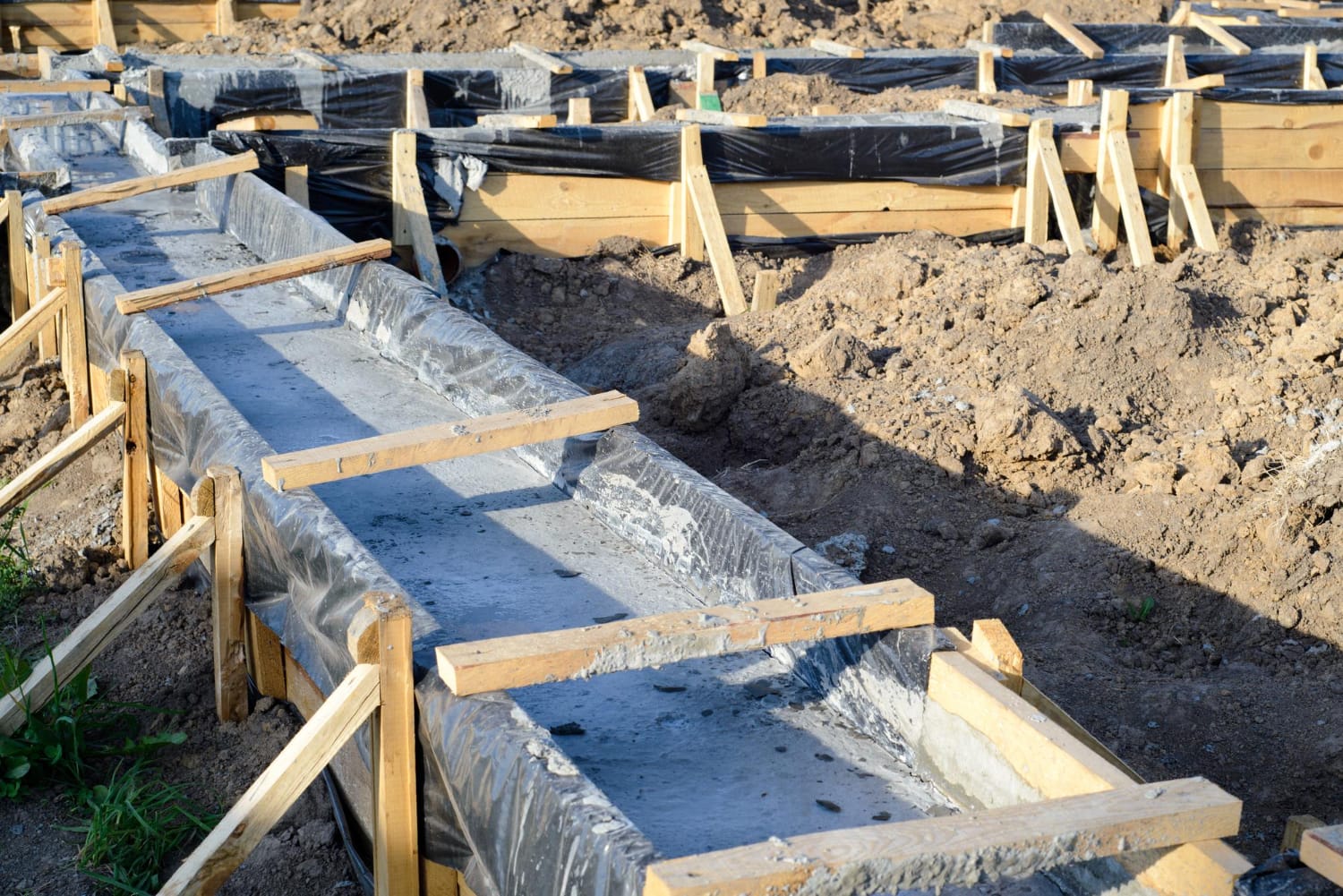 Concrete foundation being poured into wooden forms at a construction site with dirt around.