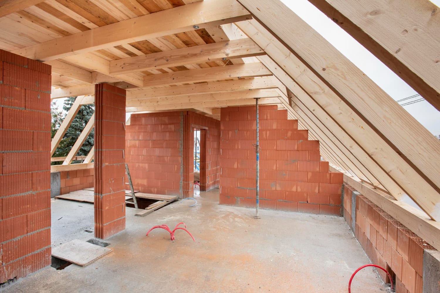 Unfinished attic space with exposed red brick walls and wooden beams, under construction.