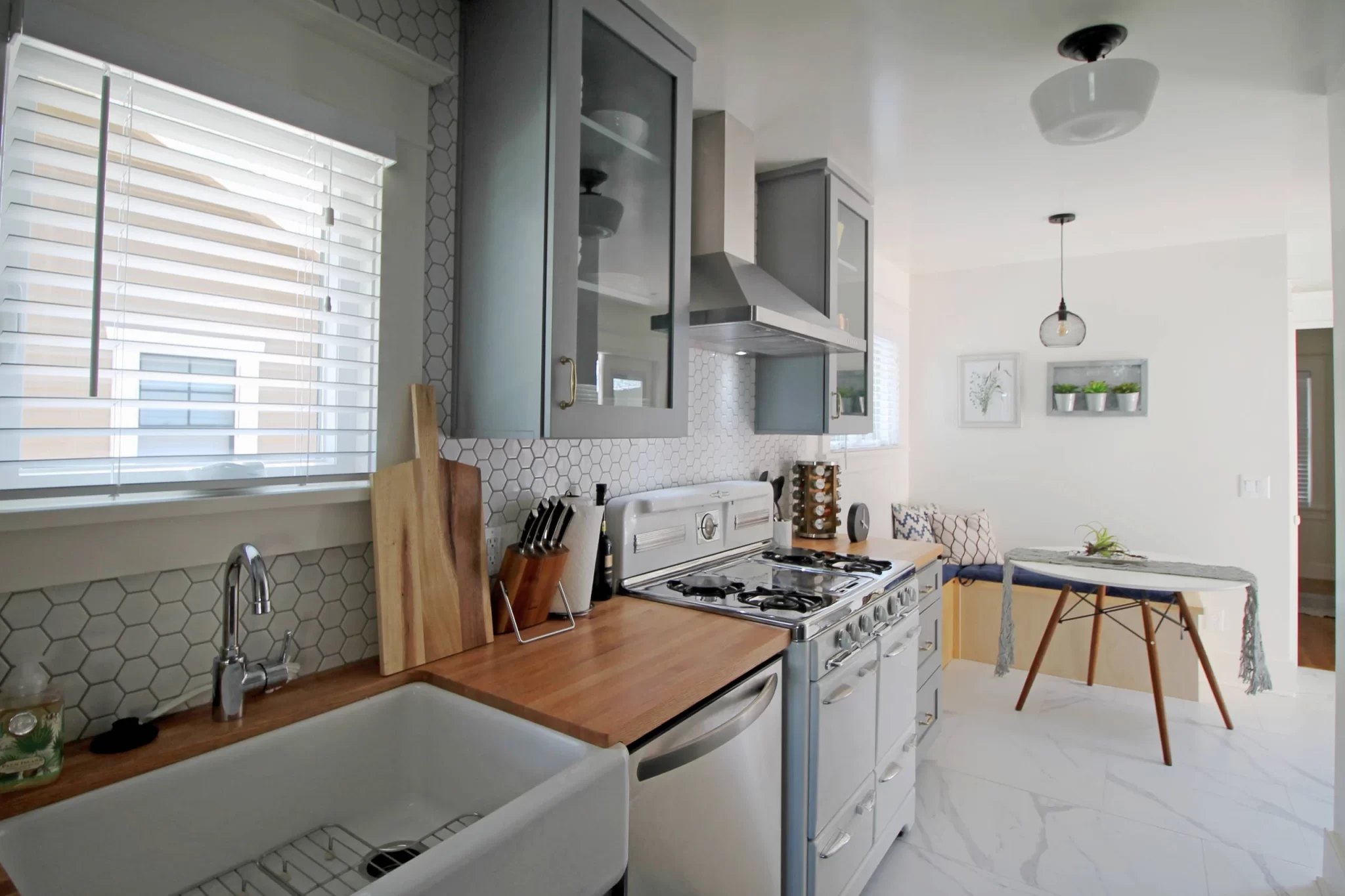 Bright, modern kitchen with gray cabinets, wood countertops, and a small dining area with bench seating.